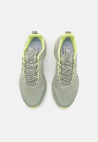Baskets de sport gris clair avec un tissu texturé, des accents verts et des détails réfléchissants ; elles sont dotées de lacets et d'un col rembourré pour le confort.