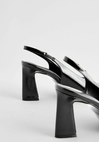Mustaa keinonahkaista slingback-kengät, joissa on neliön muotoinen kärki ja paksu korko. Ominaisuuksina kapea hihna ja sileä pinta.