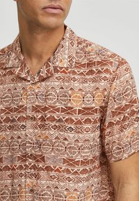 Camisa de manga corta en una tela tejida que presenta un patrón geométrico en tonos marrón y naranja, con botón en la parte delantera y diseño de cuello clásico.