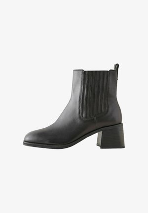 Stivale alla caviglia in pelle nera con pannelli elastici laterali, texture rigata, punta tonda e tacco a blocco. Dettagli cuciti lungo le cuciture.