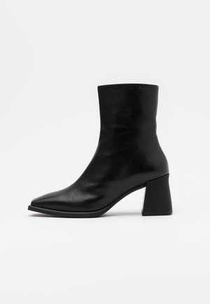 Bottine en cuir noir avec un bout pointu et un talon carré épais. Texture lisse, design minimaliste sans matériel supplémentaire.