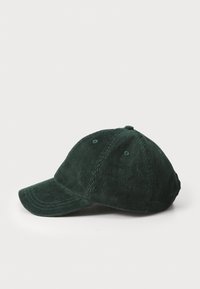 Grønn kordfløyelslue med buet skygge, teksturert stoff og seks ventilasjonshull på toppen. Klassisk baseballcapsdesign.