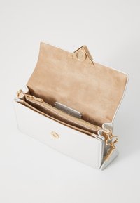 Sac à main en cuir blanc avec un intérieur en suède beige, quincaillerie dorée, fermeture magnétique et poche zippée intérieure. Accessoire en forme de cœur en porte-clés.