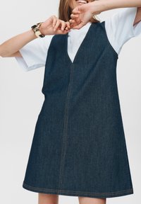 Denim jurk met een V-hals, mouwloos ontwerp en een uitlopende silhouet. Kenmerkt contrasterende oranje stiksels en een enkele zijzak.