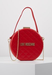 Kulatá červená prošívaná kabelka s pozlacenými detaily a řetízkovým popruhem. Na přední straně je logo 'LOVE MOSCHINO'. Hladký povrch a design pro nošení v ruce.