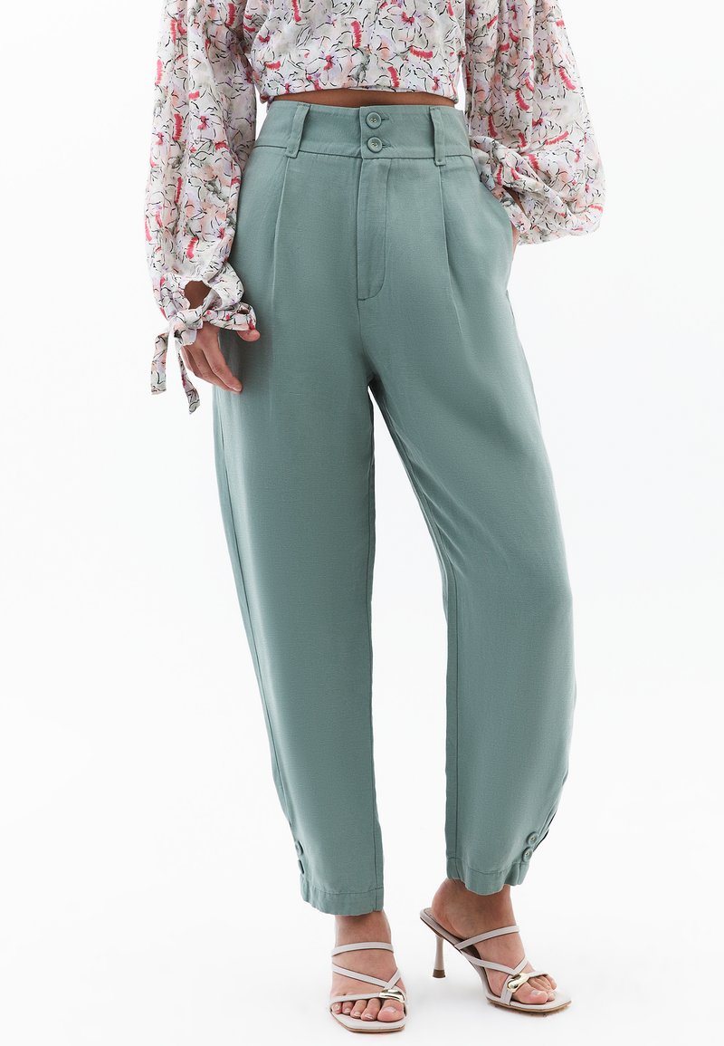 Groene, hooggetailleerde broek van gladde stof, met een dubbele knoopsluiting, zijzakken en taps toelopende pijpen.
