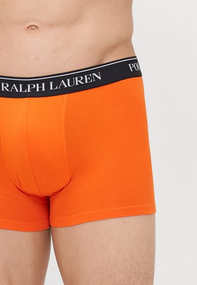 Oranžinės medvilninės bokso kelnaitės su juodu elastingu diržu, ant kurio užrašytas baltas "RALPH LAUREN" tekstas. Dizainas yra prigludęs ir lygus.
