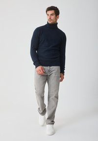 Námornícky rolák vyrobený z mäkkej látky, kombinovaný so svetlošedými džínsami a bielymi teniskami, s priliehavým strihom a rebrovanými manžetami.