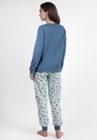 Sudadera de color azul claro con mangas largas. Pantalones de pijama estampados en azul pálido con diseños caprichosos. Dobladillos en los tobillos.