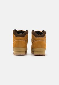 Botas de tobillo de ante marrón con acentos negros, que cuentan con un collar acolchado y una suela de goma con tacos para mejor agarre. Detalles de costura doble.