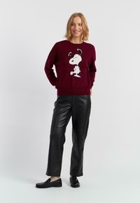 Pull bordeaux avec un design Snoopy noir et blanc. Associé à un pantalon en cuir noir et des mocassins noirs. Encolure ronde simple, manches longues.