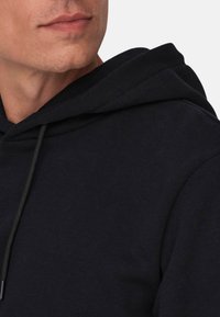 Zwarte hoodie met een trekkoord, gemaakt van zachte stof, met een ontspannen pasvorm en een gestructureerd oppervlak, met een zichtbare halslijnnaad.