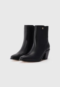 Botas de cuero negras hasta el tobillo con puntera puntiaguda, paneles laterales elásticos y un tacón de bloque geométrico. Incluye un pequeño acento de logotipo dorado.