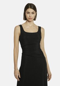 Schwarzes Kleid mit quadratischem Ausschnitt, ärmellosem Design und gerafftem Taillenbereich. Der Stoff hat eine subtile schimmernde Textur.