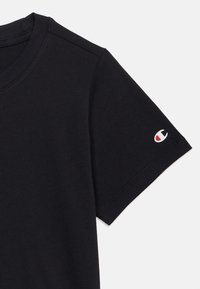 Μαύρο βαμβακερό μπλουζάκι με στρογγυλή λαιμόκοψη, κοντά μανίκια και μικρό λευκό, κόκκινο και μπλε λογότυπο στο αριστερό μανίκι. Ομαλή υφή.