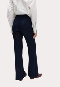 Marineblauwe pinstriped broeken met een rechte pasvorm, zijzakken en een hoge taille. Gestyled met een wit shirt enbruine schoenen.