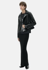 Black leather biker jacket with an asymmetrical zipper, long sleeves, and a cropped design, worn over a grey top and black skirt.