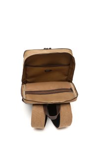 Mochila de lienzo marrón con apertura con cremallera, que cuenta con un compartimento interior, correas acolchadas y un pequeño bolsillo con cremallera para almacenamiento.