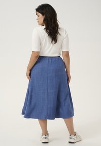 Jupe bleue, mi-longue, en tissu texturé, avec une taille élastique, associée à un haut ajusté blanc et des baskets blanches.
