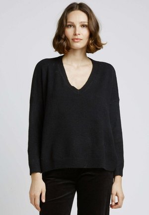 Pull oversized noir avec un col en V, des manches longues, et des bords ribbed au poignet et à l'ourlet. Texture douce, coupe décontractée et détails minimalistes.