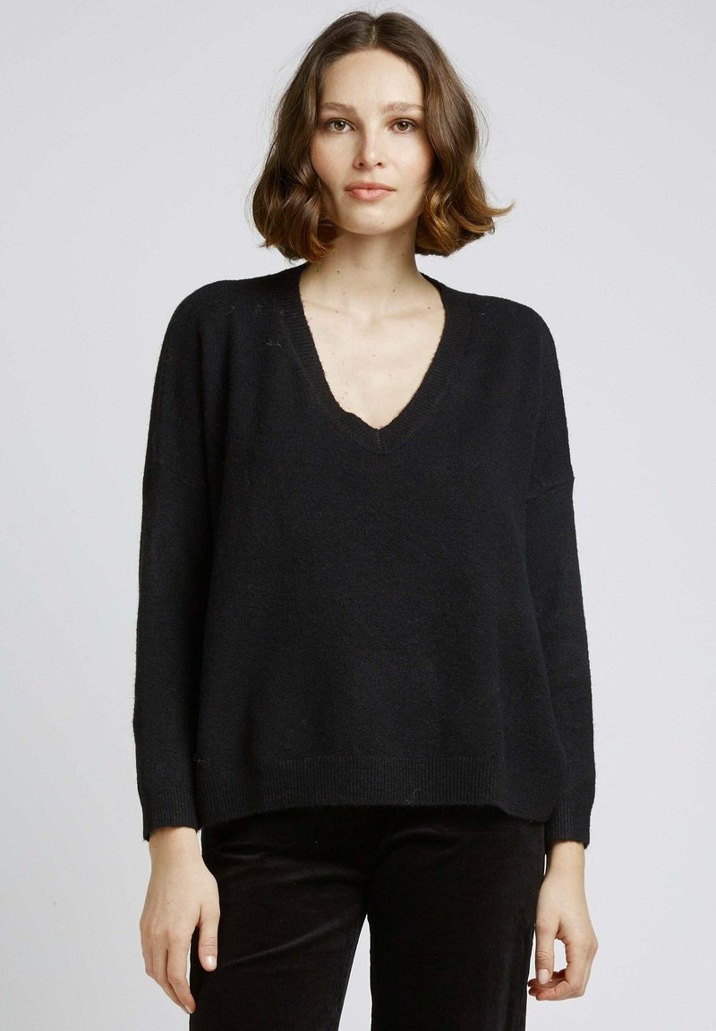 Pull oversized noir avec un col en V, des manches longues, et des bords ribbed au poignet et à l'ourlet. Texture douce, coupe décontractée et détails minimalistes.