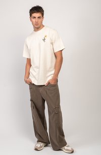 T-shirt en coton crème à manches courtes avec un petit motif. Pantalons cargo marron avec poches latérales. Baskets beige et blanches.