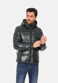 Giubbotto puffer verde scuro con finitura lucida, cappuccio e chiusura con zip. Presenta polsini elasticizzati e sezioni trapuntate per l'isolamento.
