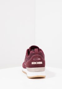 Burgundy athletic shoe with mesh and suede materials, padded collar, textured sole, and white Skechers logo on the heel.