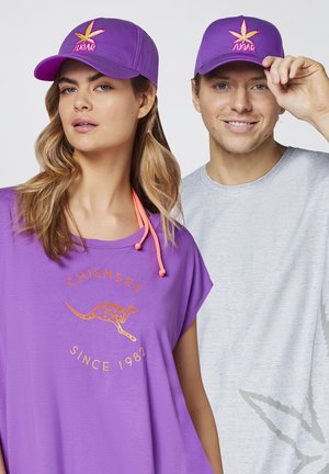 Lila Kappe mit einem Blätterlogo und dem Text "SUGAR"; Model in einem lila T-Shirt mit "CHIEMSEE" und einem Känguru-Design mit orangen Akzenten.