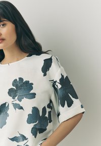 White blouse with a floral pattern featuring large navy blue flowers. Soft fabric, short sleeves, and a round neckline.