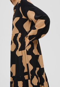 Abito a maniche lunghe con un motivo ondulato beige e nero, realizzato in tessuto morbido, con una parte inferiore svasata e un dettaglio a bottoni sul collo.