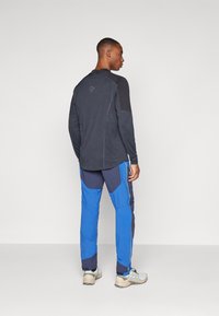 Long-sleeve dark gray top with black accents, paired with blue and navy color-blocked pants, featuring a textured fabric and reflective details.