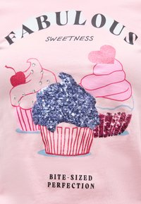 Ροζ ύφασμα με τρία διακοσμημένα κεκάκια, το ένα με μπλε παγιέτες, το ένα με κόκκινο κεράσι, και το ένα ροζ με μια καρδιά από γκλίτερ και το κείμενο «Fabulous Sweetness».