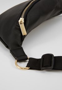 Sort lædertaske med en guldbesluttet lynlås, tekstilrem med en guldring og en glat, bøjet form.