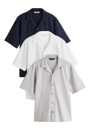 Trois chemises à manches courtes à boutons en bleu marine, blanc et gris clair, superposées et présentées sur un fond blanc.
