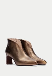 Botas de tobillo de cuero bronce metálico con punta afilada y tacón cuadrado, que cuentan con un panel lateral elástico para poner y quitar fácilmente.