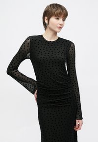 Melna kleita ar garām caurspīdīgām piedurknēm ar sirds rakstiem, krokojums gar ķermeņa daļu, apaļu apkakli un teksturētu audumu.