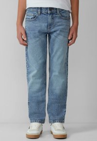 Jean en denim bleu clair avec une coupe droite, design à cinq poches et décoloration subtile ; porté avec des baskets blanches aux accents blanc cassé.
