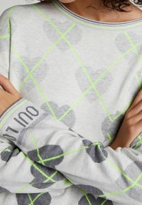 Světlounce šedý svetr s dlouhým rukávem s motivem srdce v tmavě šedé barvě, doplněný neonově zelenými linkami. Šedé pruhované manžety s nápisy.