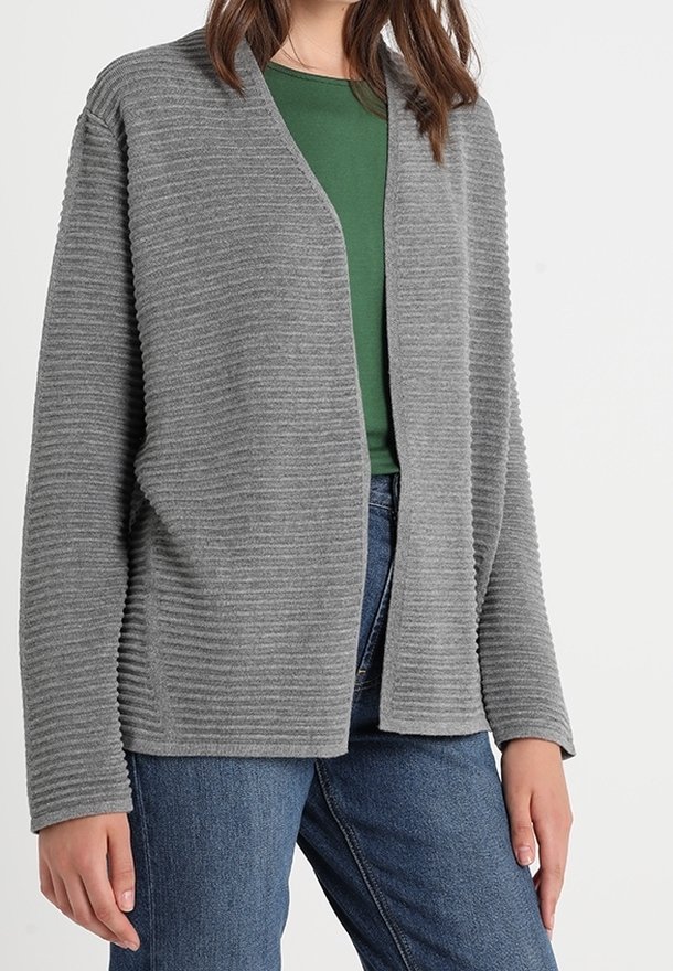Cardigan gris à côtes avec une ouverture sur le devant, des manches longues et une texture douce, porté sur un haut vert et un jean bleu.