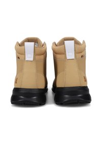 Zapatillas altas de color marrón con cuellos acolchados, tiradores blancos, suelas negras y pequeños logos en el talón vistas desde atrás sobre un fondo blanco.