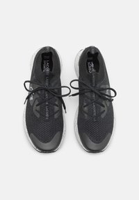 Une paire de baskets en tricot noires Lacoste avec des semelles blanches mouchetées, des lacets noirs et un logo Lacoste sur la languette et les côtés, vue de dessus.