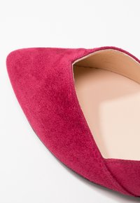 Chaussure plate à bout pointu avec tige en suède bordeaux profond et doublure intérieure beige clair sur fond blanc.