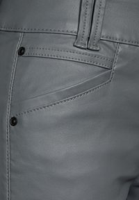 Grå konstläderbyxor med slät yta, synliga sömmar och svarta metallaccenter. Har en framficka och bälteshällor.