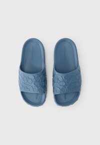 Blaue Gummischlappen verfügen über einen breiten Riemen mit eingeprägten Kreis-Mustern und eine flache Sohle. Das Design ist minimalistisch mit einer glatten Textur.