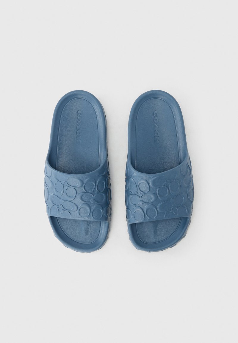 Blaue Gummischlappen verfügen über einen breiten Riemen mit eingeprägten Kreis-Mustern und eine flache Sohle. Das Design ist minimalistisch mit einer glatten Textur.