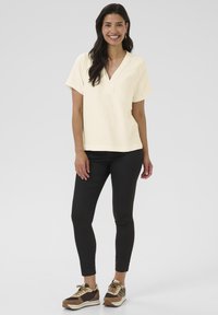 Haut court à manches courtes de couleur jaune clair avec un décolleté en V et un tissu texturé, associé à des leggings noirs et des baskets brunes avec des accents beiges.