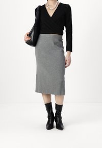 Svart wrap-top, grå ribbad kjol ovanför knäet, svarta läderstövlar i slouchy stil, accessoriserad med lager av halsband och en svart handväska.