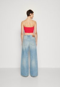 Červený bezramínkový crop top v kombinaci se světle modrými širokými džíny, které mají vybledlou strukturu a malou koženou nášivku na zadní straně.