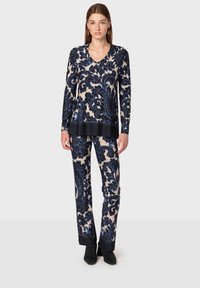 Långärmad topp och byxor i krämfärg med mörkblå paisleymönster, med V-ringning och svarta enfärgade detaljer vid fållen.